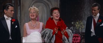 Movie still from “Auntie Mame” (1958), directed by Morton DaCosta – Two women are laughing together in a scene from a movie; Medium shot, Low angle