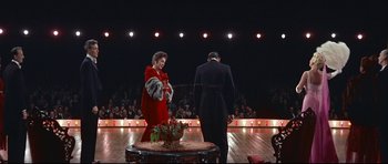 Movie still from “Auntie Mame” (1958), directed by Morton DaCosta – A man and a woman are standing in front of an audience; Wide shot, High angle