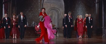 Movie still from “Auntie Mame” (1958), directed by Morton DaCosta – A woman in a red dress is holding a pink shawl; Wide shot, Low angle