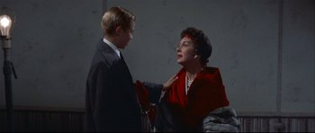 Movie still from “Auntie Mame” (1958), directed by Morton DaCosta – An older woman in a red dress talking to a young man in a black suit; Medium shot, Low angle