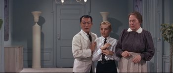 Movie still from “Auntie Mame” (1958), directed by Morton DaCosta – Two men and a woman standing next to each other in a room; Medium shot, Low angle