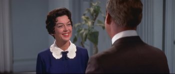 Movie still from “Auntie Mame” (1958), directed by Morton DaCosta – A woman in a blue dress smiles at a man in a brown suit; Medium shot, Over the shoulder angle