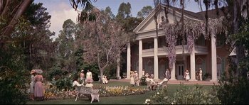 Movie still from “Auntie Mame” (1958), directed by Morton DaCosta – A group of people sitting in front of a large house; Extreme Wide shot, High angle