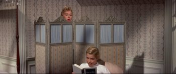 Movie still from “Auntie Mame” (1958), directed by Morton DaCosta – A young boy reading a book in front of a woman; Medium shot, Over the shoulder angle