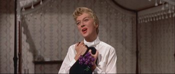 Movie still from “Auntie Mame” (1958), directed by Morton DaCosta – A woman in a white shirt holding a black and purple bouquet of flowers; Medium shot, Low angle