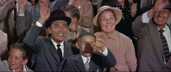 Movie still from “Auntie Mame” (1958), directed by Morton DaCosta – An older man and a younger man and a woman wave at the camera; Medium shot, Low angle