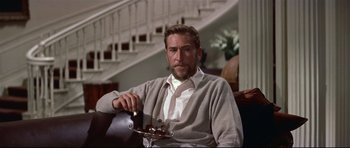 Movie still from “Auntie Mame” (1958), directed by Morton DaCosta – A man sitting in a chair holding a tray of food; Medium shot, Low angle