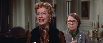 Movie still from “Auntie Mame” (1958), directed by Morton DaCosta – A woman with red lipstick standing next to another woman; Medium shot, Over the shoulder angle