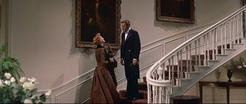 Movie still from “Auntie Mame” (1958), directed by Morton DaCosta – A man and a woman standing next to each other on a staircase; Wide shot, Low angle