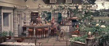 Movie still from “Auntie Mame” (1958), directed by Morton DaCosta – A man and a woman sitting at a bar in front of an oven; Wide shot, High angle