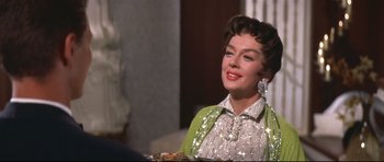 Movie still from “Auntie Mame” (1958), directed by Morton DaCosta – A woman in a sequined dress smiles while holding a tray; Close Up shot, Over the shoulder angle