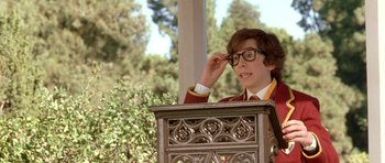 Movie still from “Austin Powers in Goldmember” (2002), directed by Jay Roach – A young man wearing glasses standing in front of an ornate screen; Medium shot, Over the shoulder angle