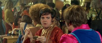 Movie still from “Austin Powers in Goldmember” (2002), directed by Jay Roach – A man in a red and gold outfit looking at a cell phone; Close Up shot, Over the shoulder angle