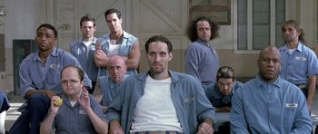 Movie still from “Austin Powers in Goldmember” (2002), directed by Jay Roach – A group of men sitting next to each other in front of a barn; Medium shot, Low angle