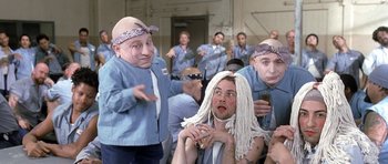 Movie still from “Austin Powers in Goldmember” (2002), directed by Jay Roach – A group of people in a room with a man with a wig; Medium shot, Low angle