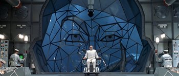 Movie still from “Austin Powers in Goldmember” (2002), directed by Jay Roach – A man sitting in a chair in front of a giant face; Wide shot, Low angle