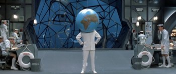 Movie still from “Austin Powers in Goldmember” (2002), directed by Jay Roach – A man in a white suit standing next to a blue globe; Wide shot, High angle