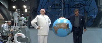 Movie still from “Austin Powers in Goldmember” (2002), directed by Jay Roach – A man in a white suit standing next to a blue globe; Medium shot, Low angle