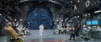 Movie still from “Austin Powers in Goldmember” (2002), directed by Jay Roach – A man standing in front of a wall with an image on it; Extreme Wide shot, High angle