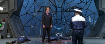 Movie still from “Austin Powers in Goldmember” (2002), directed by Jay Roach – A man standing in front of a man laying on the ground; Wide shot, Over the shoulder angle