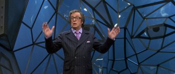 Movie still from “Austin Powers in Goldmember” (2002), directed by Jay Roach – A man in a suit and tie standing in front of a building; Medium shot, Low angle