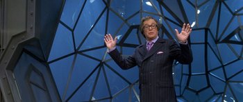 Movie still from “Austin Powers in Goldmember” (2002), directed by Jay Roach – A man wearing a suit and tie standing in front of a glass wall; Medium shot, Low angle