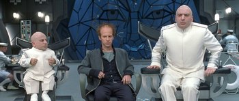 Movie still from “Austin Powers in Goldmember” (2002), directed by Jay Roach – A man sitting in a chair in front of another man; Medium shot, Low angle