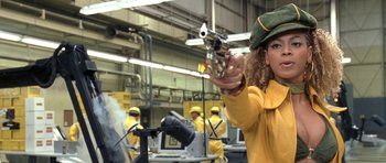 Movie still from “Austin Powers in Goldmember” (2002), directed by Jay Roach – A woman in a yellow jacket holding a gun in a factory; Medium shot, Low angle