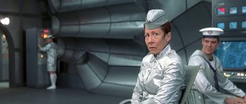 Movie still from “Austin Powers in Goldmember” (2002), directed by Jay Roach – An older woman wearing a silver uniform sitting on a chair; Medium shot, Over the shoulder angle