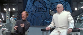 Movie still from “Austin Powers in Goldmember” (2002), directed by Jay Roach – Two men sitting next to each other in front of a wall; Medium shot, Over the shoulder angle