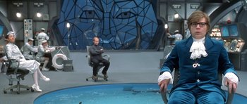 Movie still from “Austin Powers in Goldmember” (2002), directed by Jay Roach – A man sitting in a chair in front of a pool; Medium shot, Over the shoulder angle