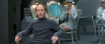 Movie still from “Austin Powers in Goldmember” (2002), directed by Jay Roach – A man sitting in a chair in front of a woman in a suit; Medium shot, Over the shoulder angle