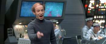 Movie still from “Austin Powers in Goldmember” (2002), directed by Jay Roach – A man in a gray sweater is talking to someone in front of a television; Close Up shot, Low angle