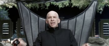 Movie still from “Austin Powers in Goldmember” (2002), directed by Jay Roach – A bald man sitting in a chair with his mouth wide open; Medium shot, High angle