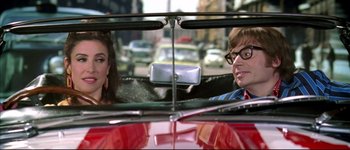 Movie still from “Austin Powers: International Man of Mystery” (1997), directed by Jay Roach – A man and a woman sitting in the back seat of a red car; Medium shot, Over the shoulder angle