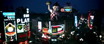 Movie still from “Austin Powers: International Man of Mystery” (1997), directed by Jay Roach – A large statue of a man holding a hamburger on top of a building; Extreme Wide shot, High angle