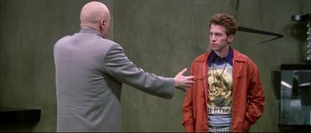 Movie still from “Austin Powers: International Man of Mystery” (1997), directed by Jay Roach – A man is talking to another man on stage; Medium shot, Over the shoulder angle