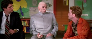 Movie still from “Austin Powers: International Man of Mystery” (1997), directed by Jay Roach – A bald man sitting in a room holding a nintendo wii game controller; Medium shot, Low angle