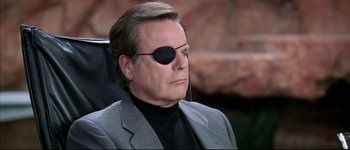 Movie still from “Austin Powers: International Man of Mystery” (1997), directed by Jay Roach – A man wearing a suit and eye patch sitting down; Close Up shot, Over the shoulder angle