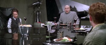 Movie still from “Austin Powers: International Man of Mystery” (1997), directed by Jay Roach – A man sitting at a table with a plate of food in front of him; Medium shot, Over the shoulder angle