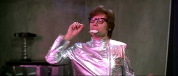 Movie still from “Austin Powers: International Man of Mystery” (1997), directed by Jay Roach – A man in a silver suit is eating something; Medium shot, Low angle