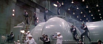 Movie still from “Austin Powers: International Man of Mystery” (1997), directed by Jay Roach – A group of people in black and white suits standing on top of an object in a building; Extreme Wide shot, Low angle