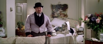 Movie still from “Austin Powers: International Man of Mystery” (1997), directed by Jay Roach – A man standing in front of a bed with a tray of silverware; Medium shot, Low angle