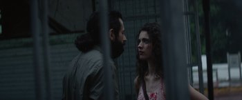 Movie still from “Stars at Noon” (2022), directed by Claire Denis – A man and a woman standing next to each other in front of a fence; Close Up shot, Over the shoulder angle