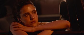 Movie still from “Stars at Noon” (2022), directed by Claire Denis – A beautiful young lady sitting on top of a couch; Close Up shot, Over the shoulder angle