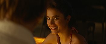 Movie still from “Stars at Noon” (2022), directed by Claire Denis – A beautiful woman smiling at the camera in the dark; Close Up shot, Over the shoulder angle