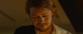 Movie still from “Stars at Noon” (2022), directed by Claire Denis – A person wearing a suit and beard; Close Up shot, Over the shoulder angle