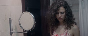 Movie still from “Stars at Noon” (2022), directed by Claire Denis – A woman standing in front of a round mirror; Close Up shot, Over the shoulder angle