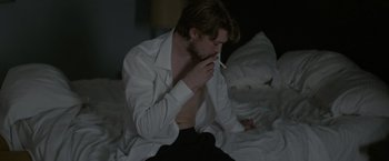 Movie still from “Stars at Noon” (2022), directed by Claire Denis – A man sitting on a bed with a cigarette in his mouth; Medium shot, High angle