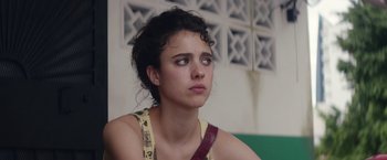 Movie still from “Stars at Noon” (2022), directed by Claire Denis – A woman sitting in front of a green wall looking sad; Close Up shot, Over the shoulder angle